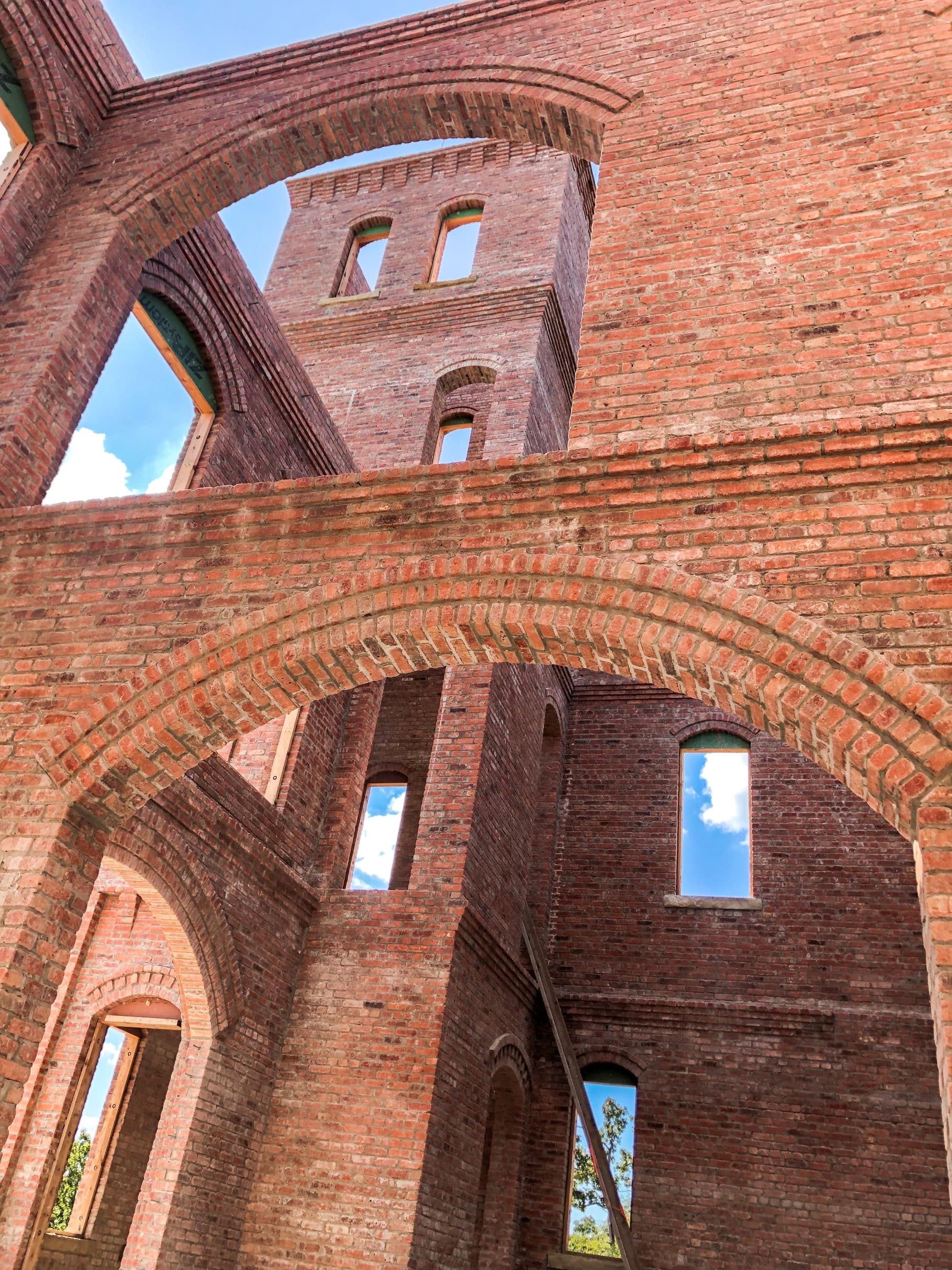 Looking up through structural brick masonry — towers under construction with exposed arches and clear sky between them