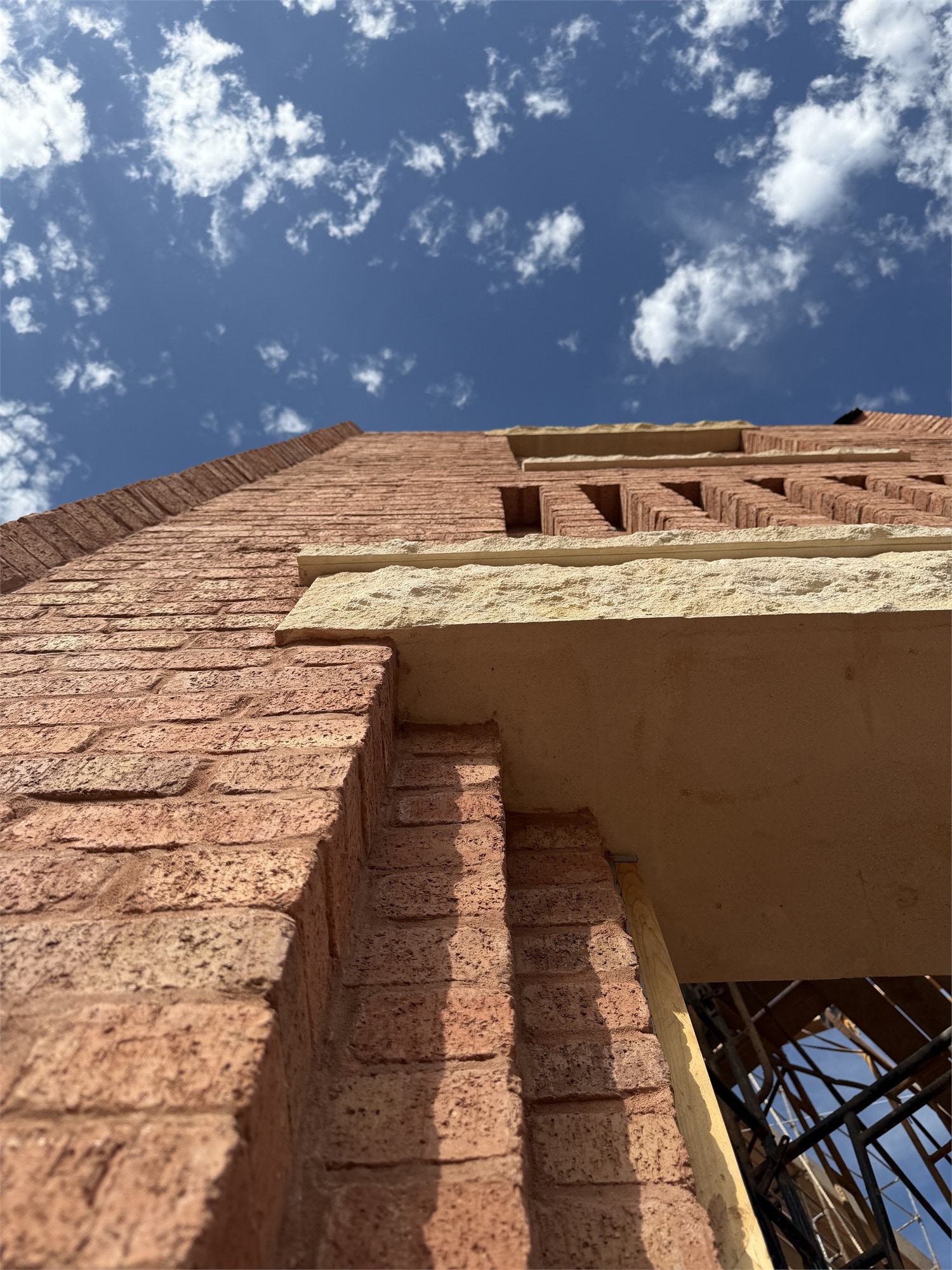 Looking up at the corner of an Apollo Workspace building during construction — brick cornice against blue sky.