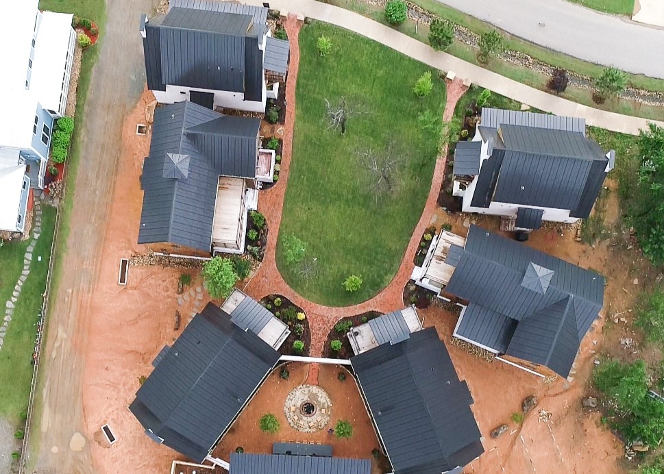 Aerial view of a Building Culture neighborhood — homes with standing-seam roofs arranged around a shared green courtyard and brick walkways.