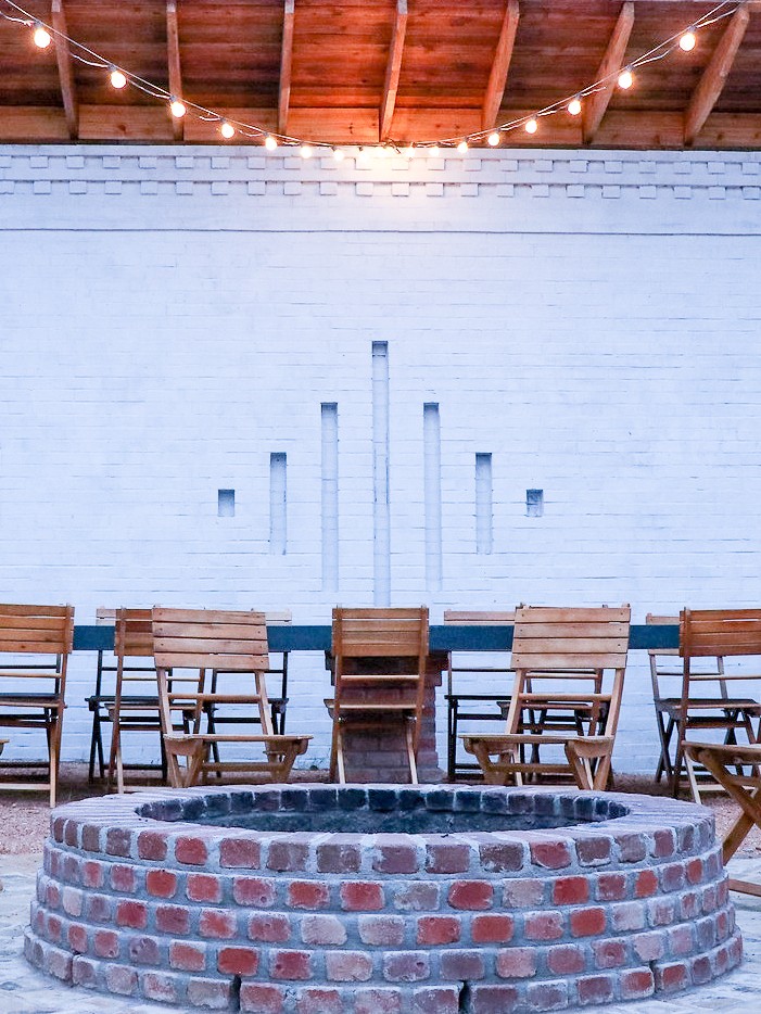 The fire-pit gathering courtyard at The Bend at Carlton Landing — wooden chairs around a long communal table with string lights overhead.