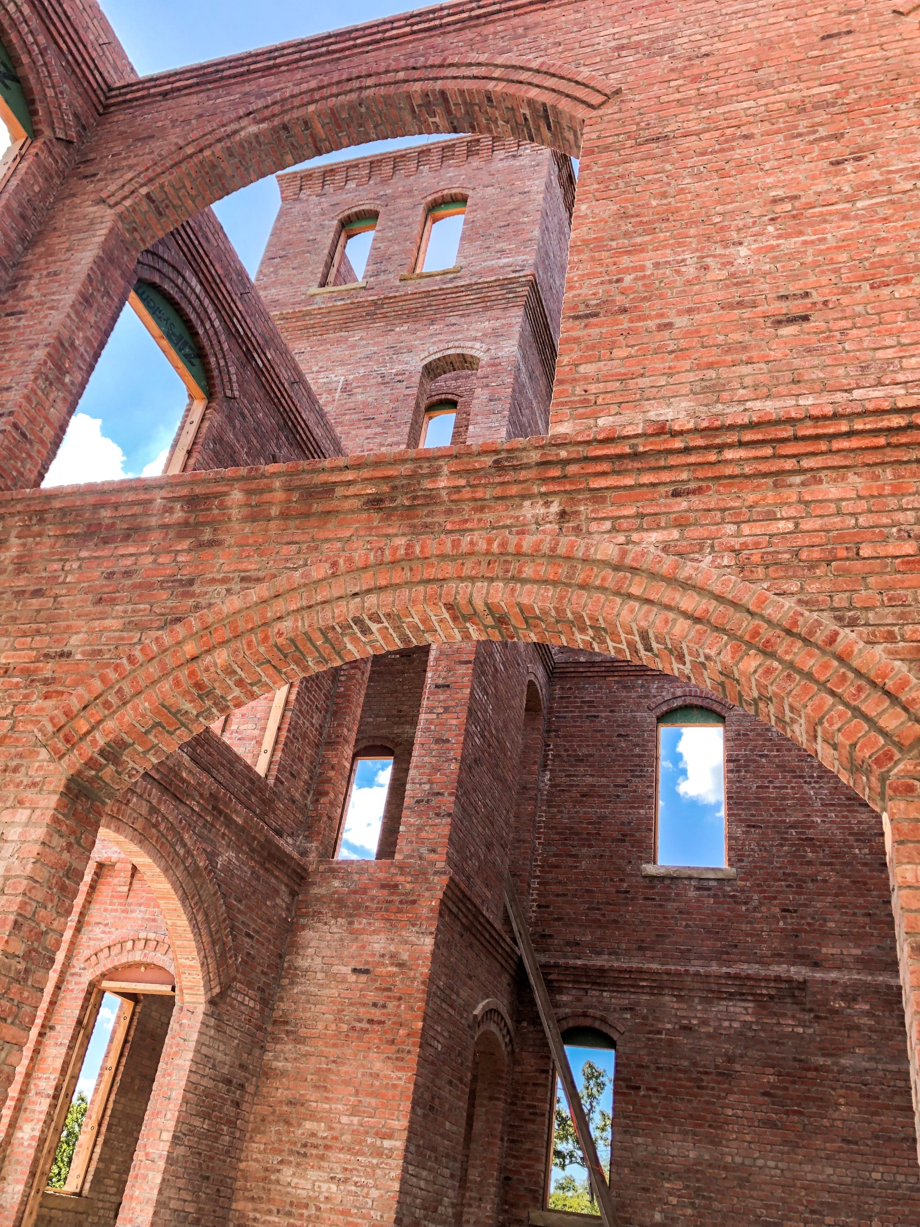 Looking up through structural brick masonry — towers under construction with exposed arches and clear sky between them.