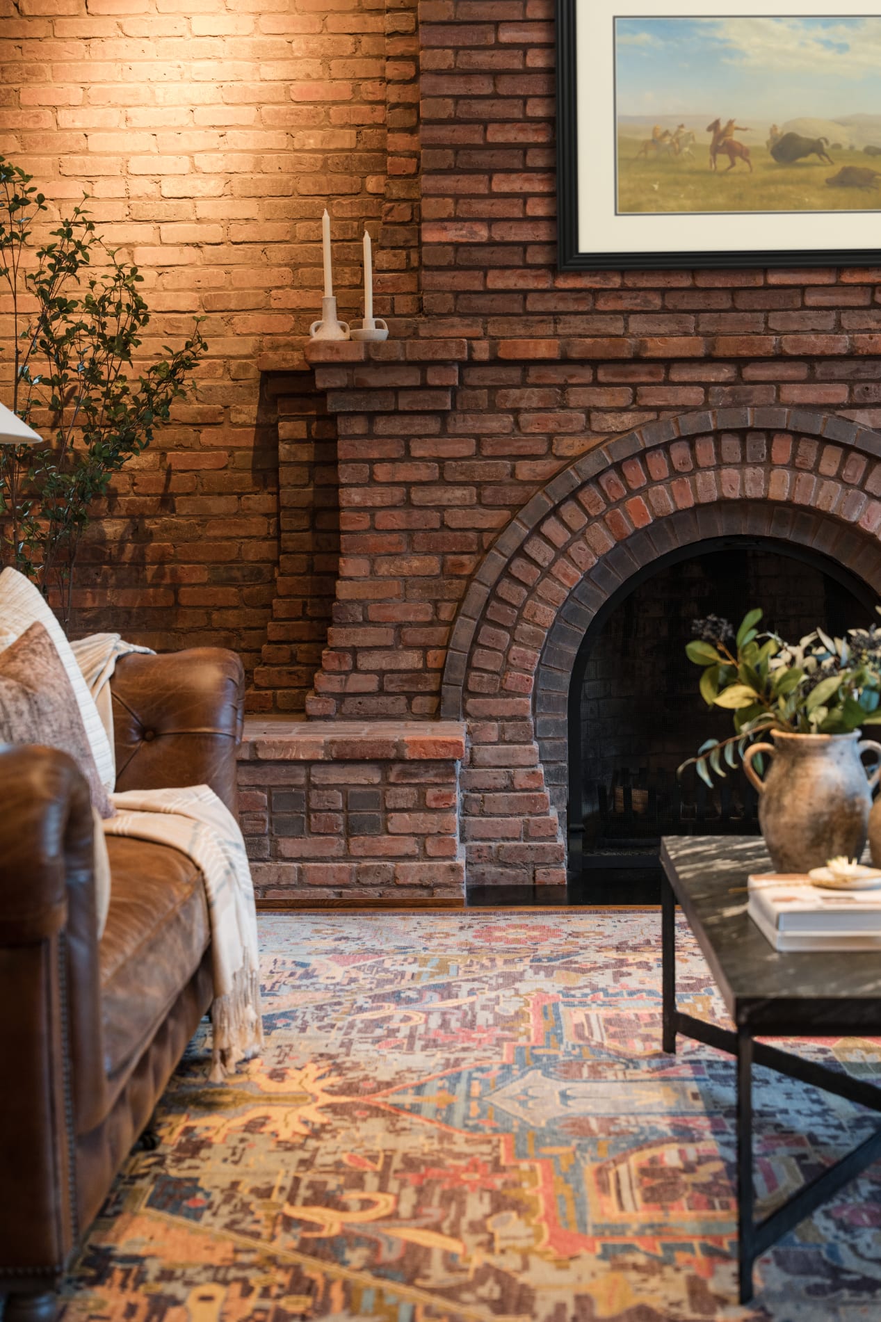 Living room interior with a brick arched fireplace, leather chesterfield sofa, vintage Persian rug, and a period plains painting on the brick.