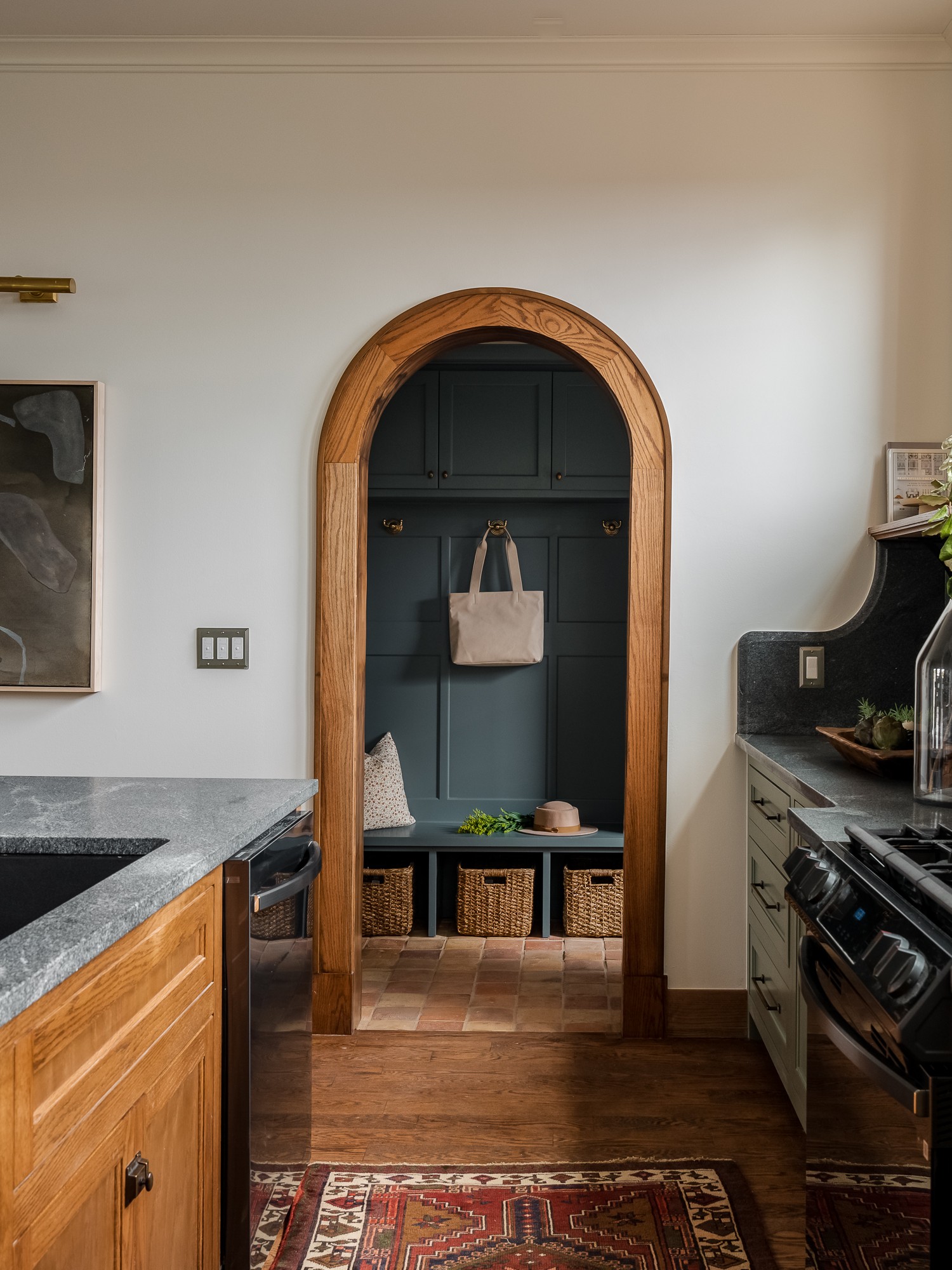 Kitchen interior with an oak-trimmed arched mudroom doorway, soapstone counters, olive cabinets, and period architectural detailing.
