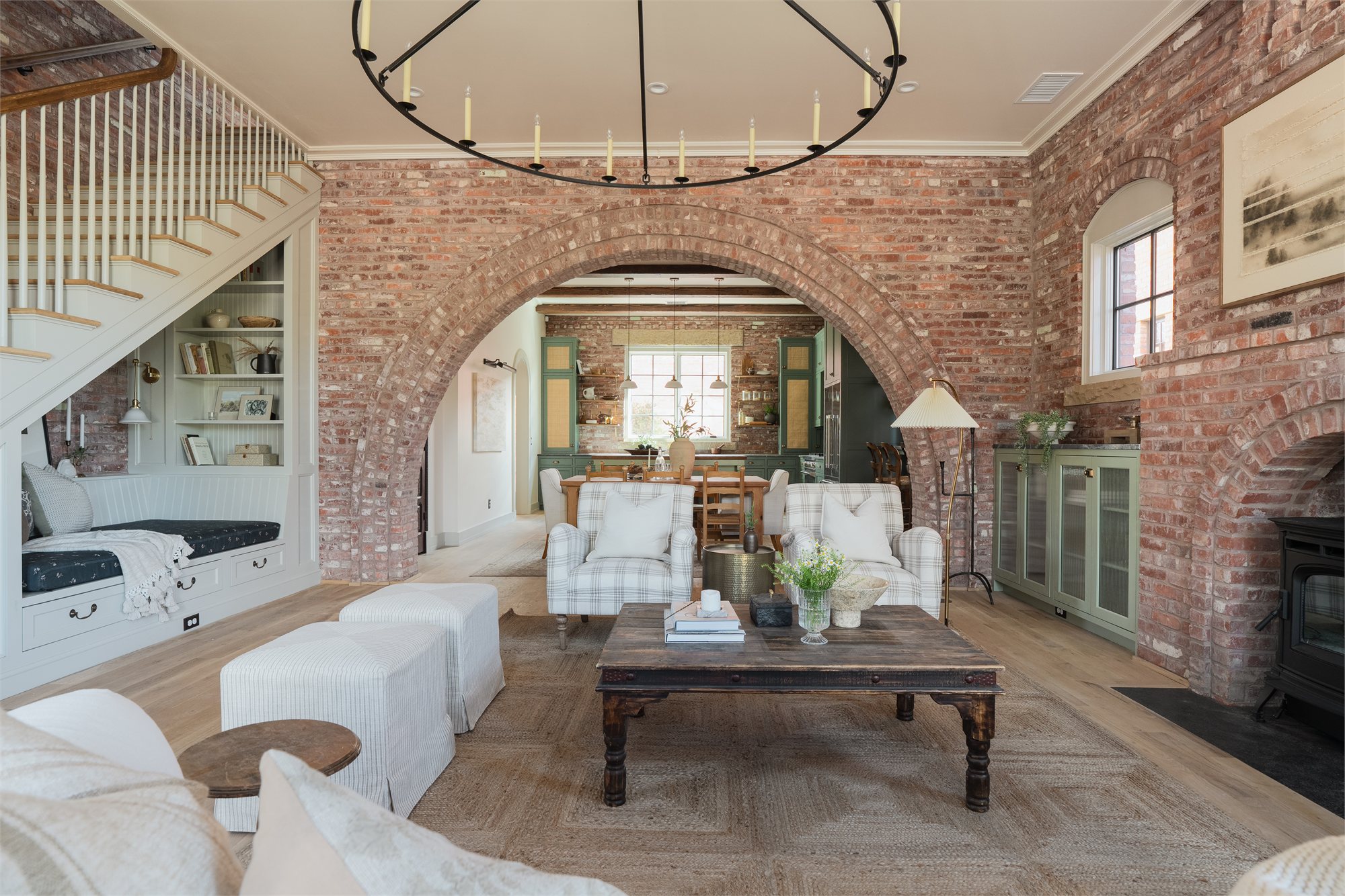 Living room with a brick archway, iron candle chandelier, slipcovered seating, and an exposed brick reading nook.