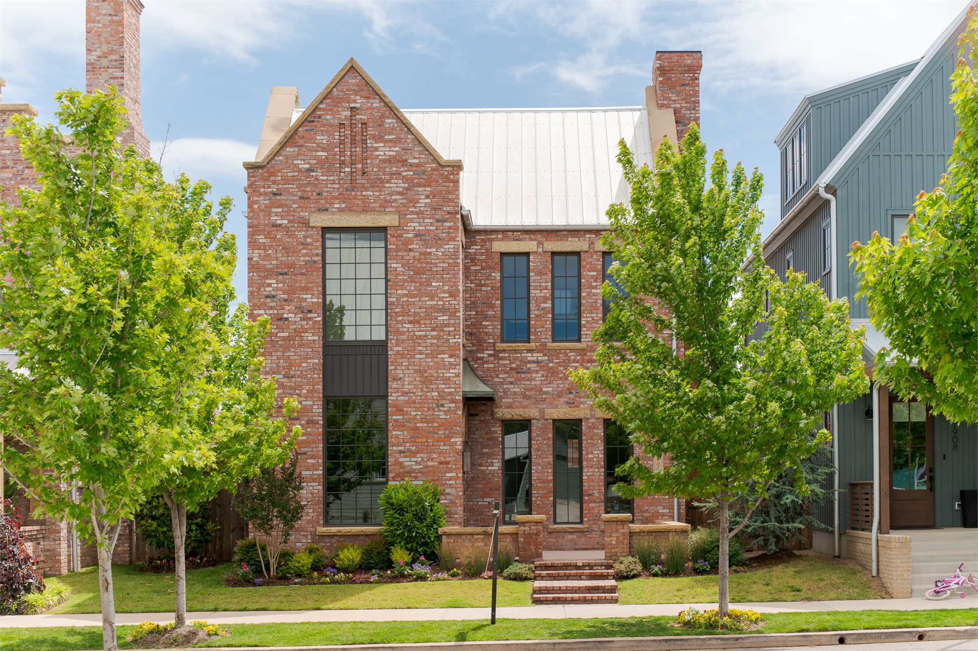 Steep-gabled brick elevation — tall mullioned window, standing-seam metal roof, set among trees.