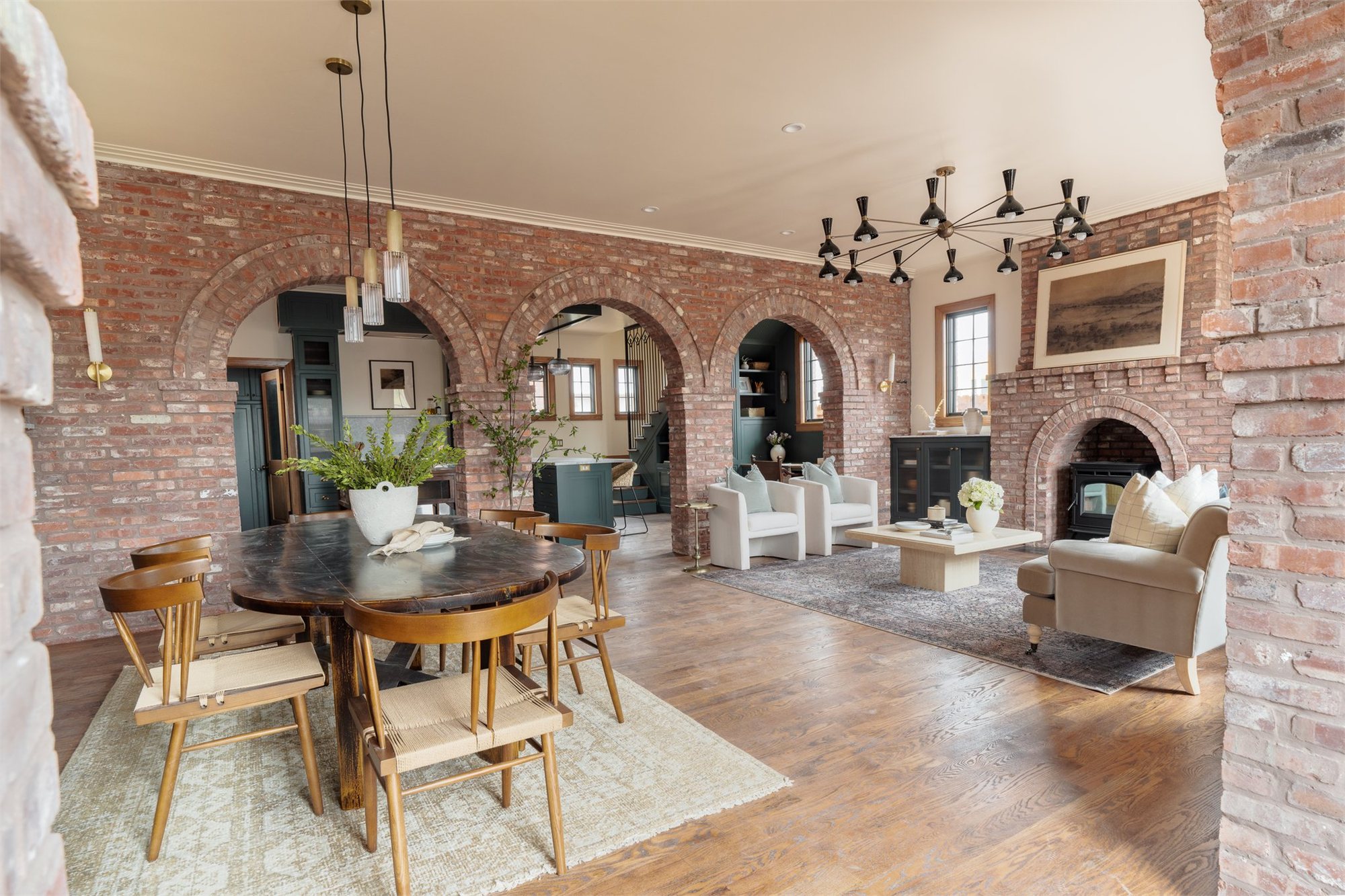 Open-plan interior — three brick arches divide dining, living, and a recessed hearth under exposed beams.