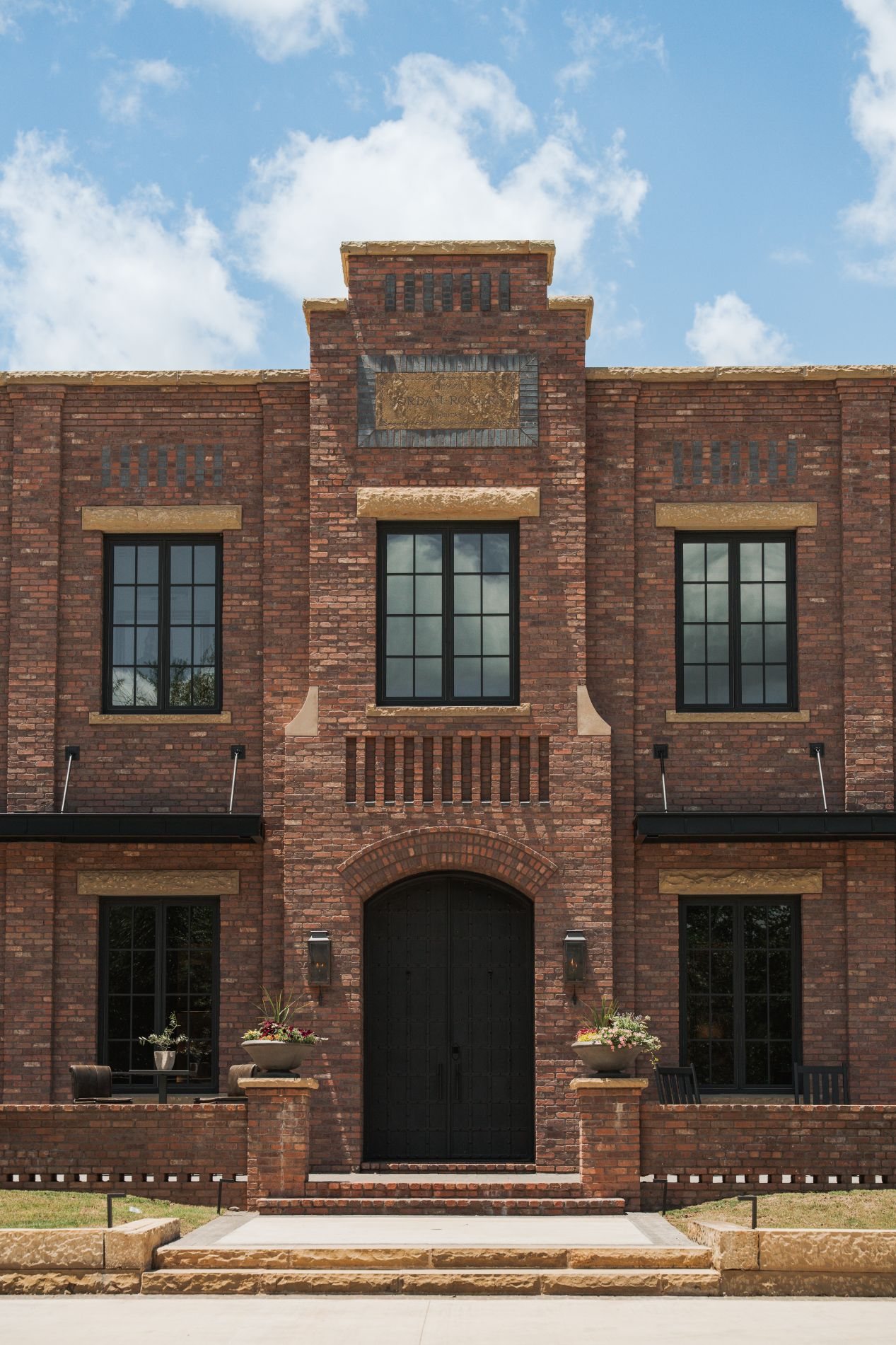 Symmetrical brick facade — sandstone-banded windows, central parapet, dark double-leaf entry under a brick arch.