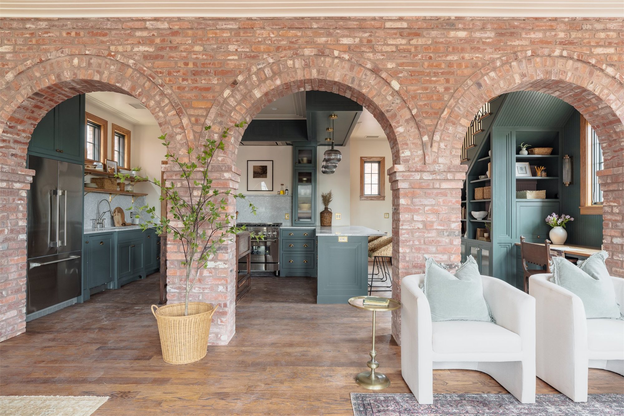 Three brick arches opening into a sage-cabinet kitchen with brick walls and timber detail.