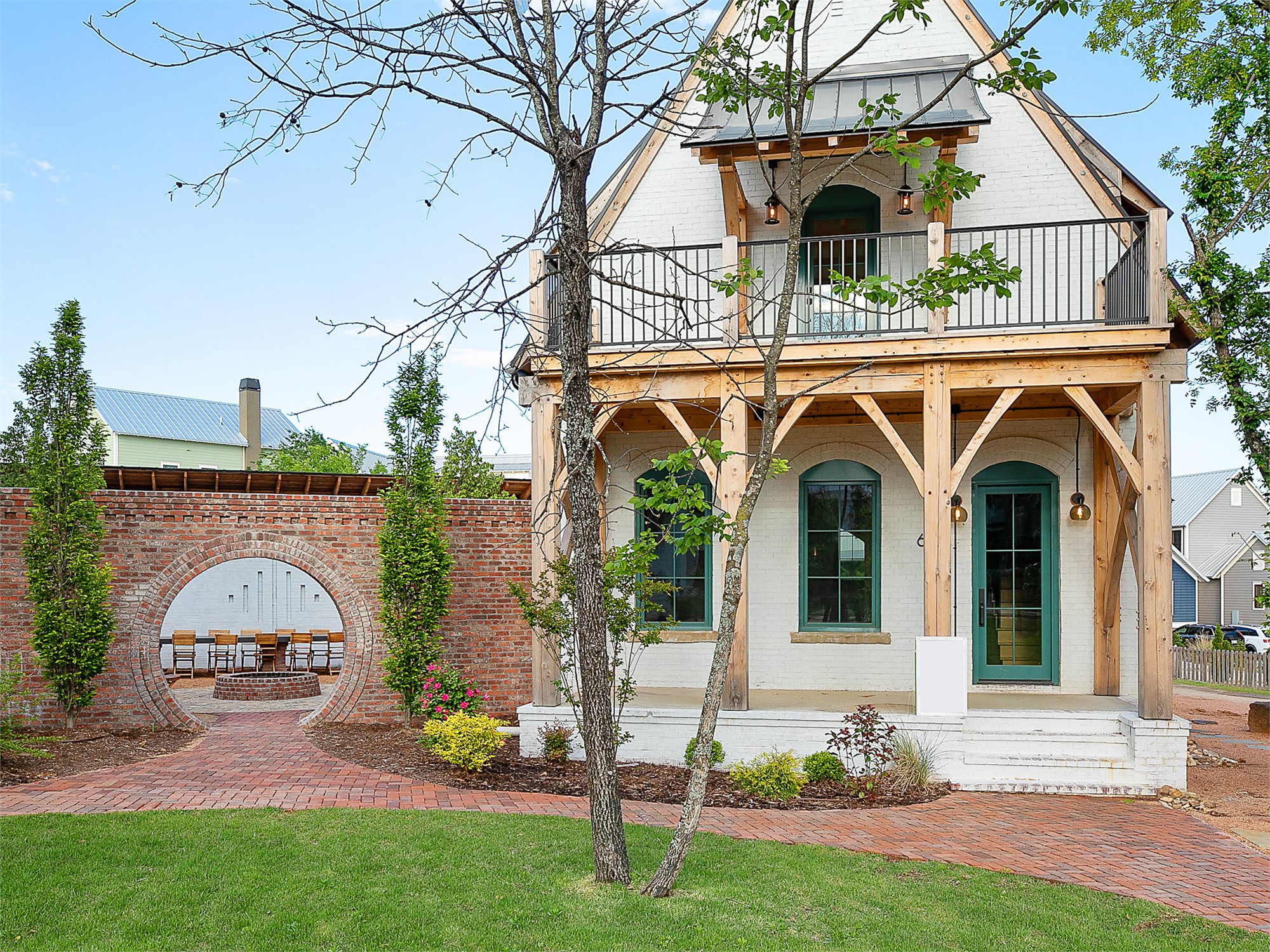 A cottage at The Bend at Carlton Landing — white-painted brick, peaked gable with a timber-frame porch, and a circular brick moon-gate set into the garden wall.