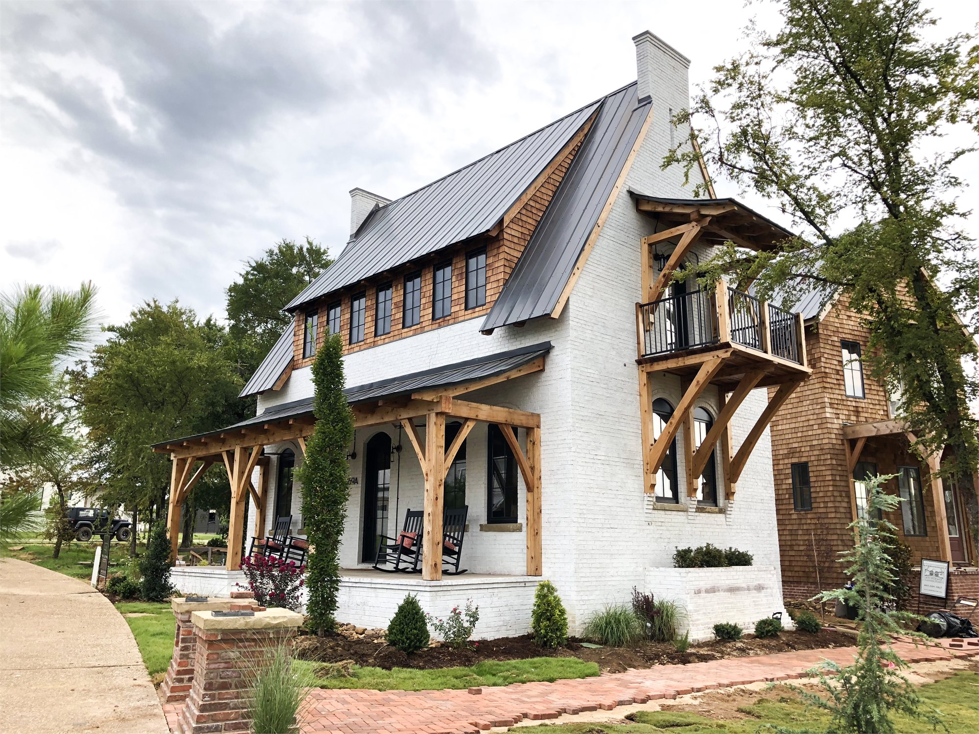 Cottage exterior with white-painted brick, cedar shake gable, and a full-width timber-frame porch and balcony.