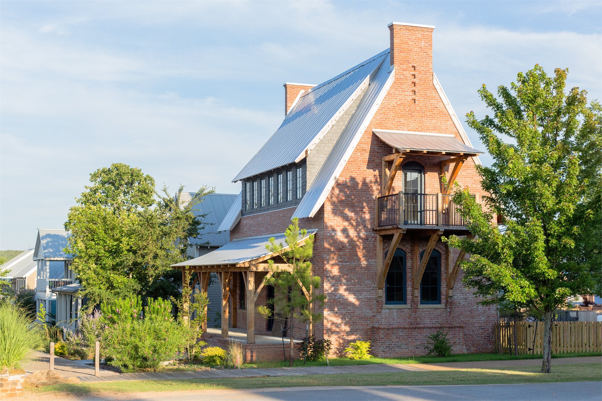 A red-brick cottage with a standing-seam metal roof, timber-frame side porch, and mature landscaping.