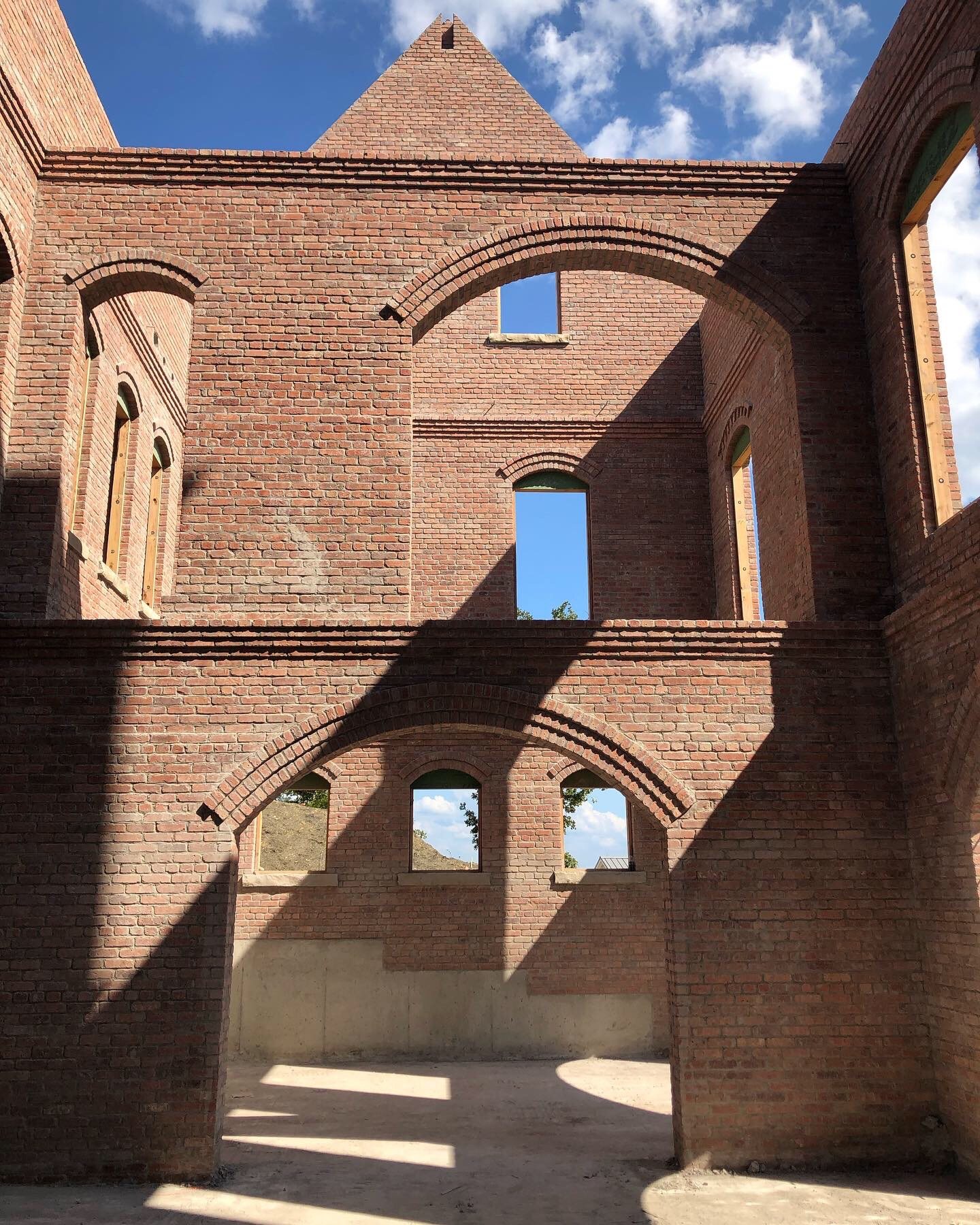 Structural masonry shell during construction — brick walls and arched openings open to the sky, raking afternoon shadow.