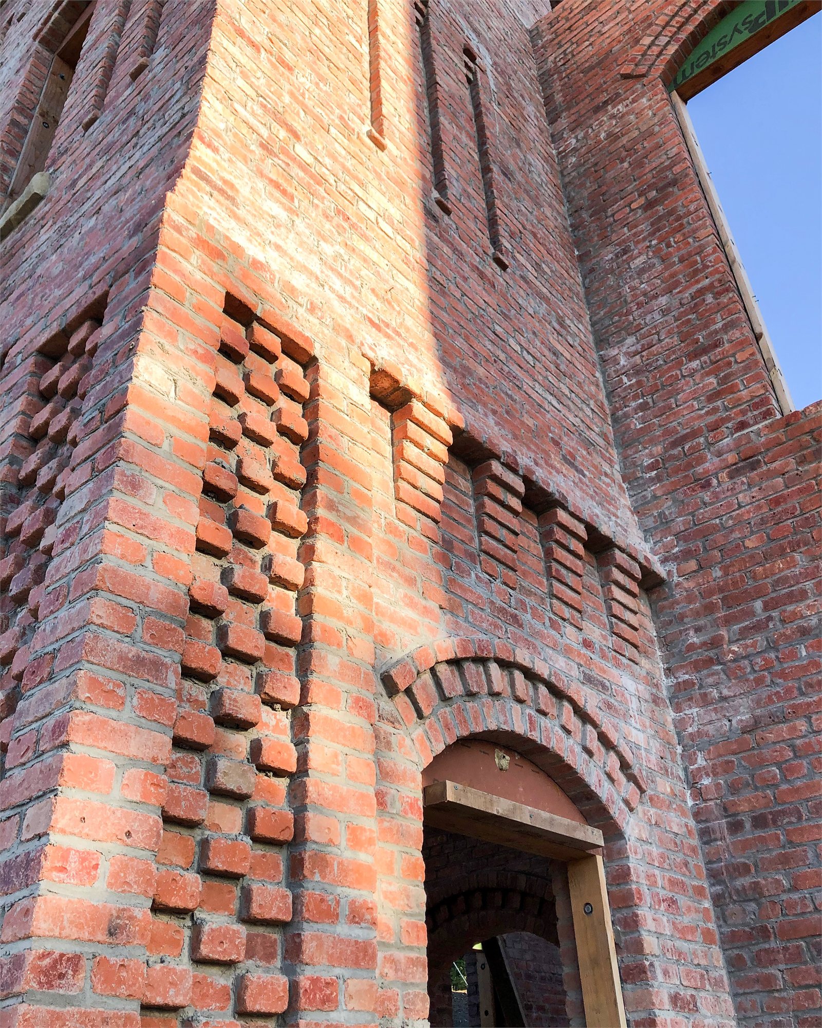 Detail of a structural brick masonry tower — corbeled cornice and brick-lattice ventilation panels above an arched entry.