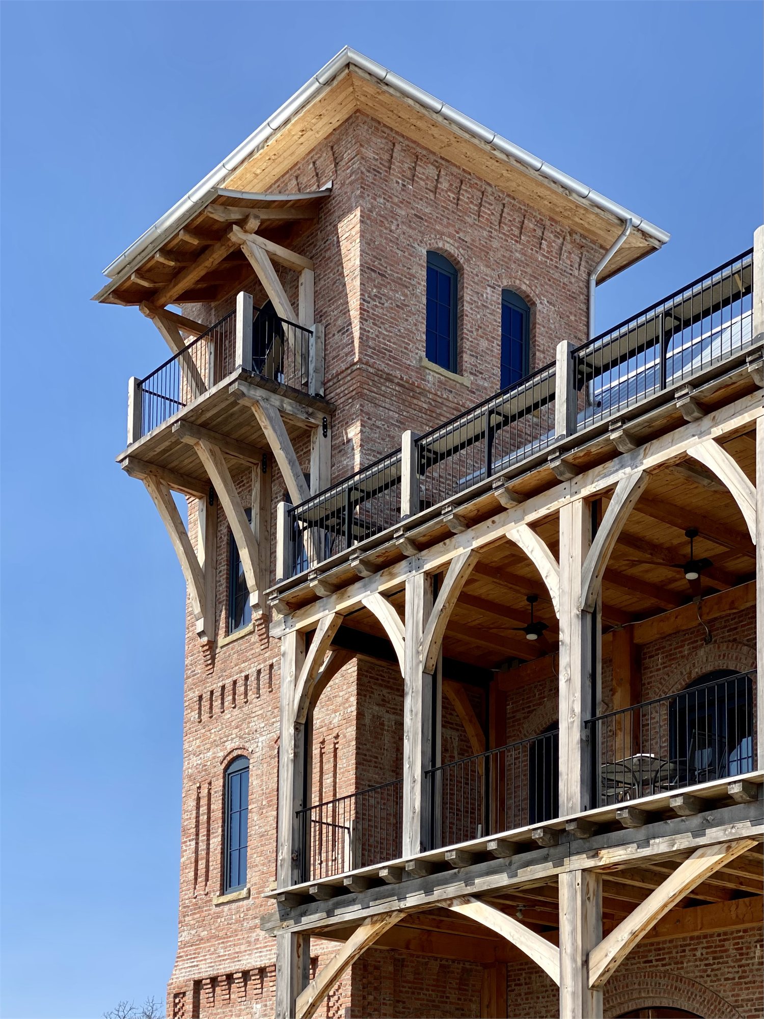 A masonry tower at Selah with a timber-frame balcony — brick walls, arched window bays, exposed knee braces.