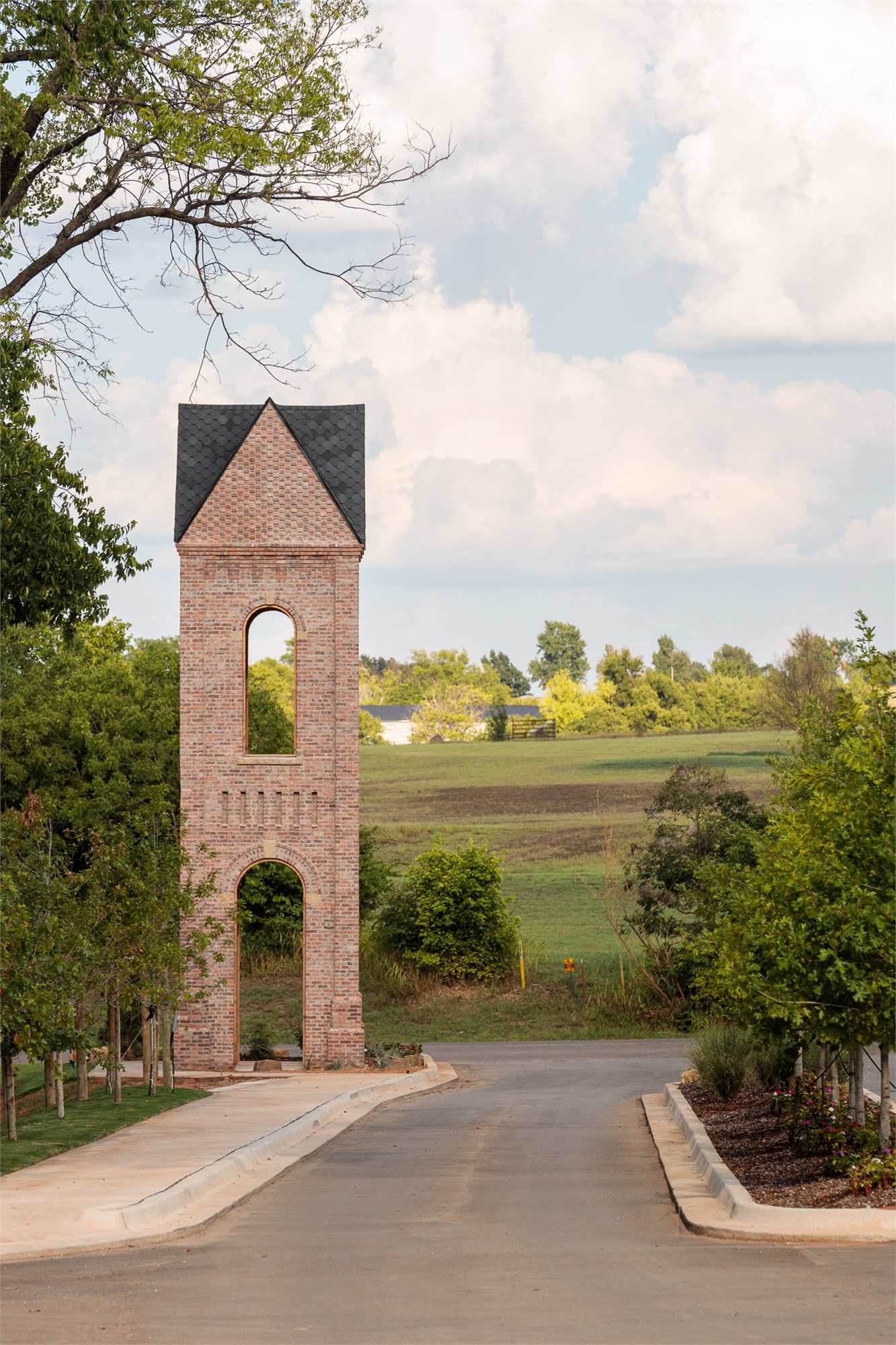 Selah's brick bell-tower at the end of an entry road — pitched slate roof, masonry plinth, rolling landscape beyond.