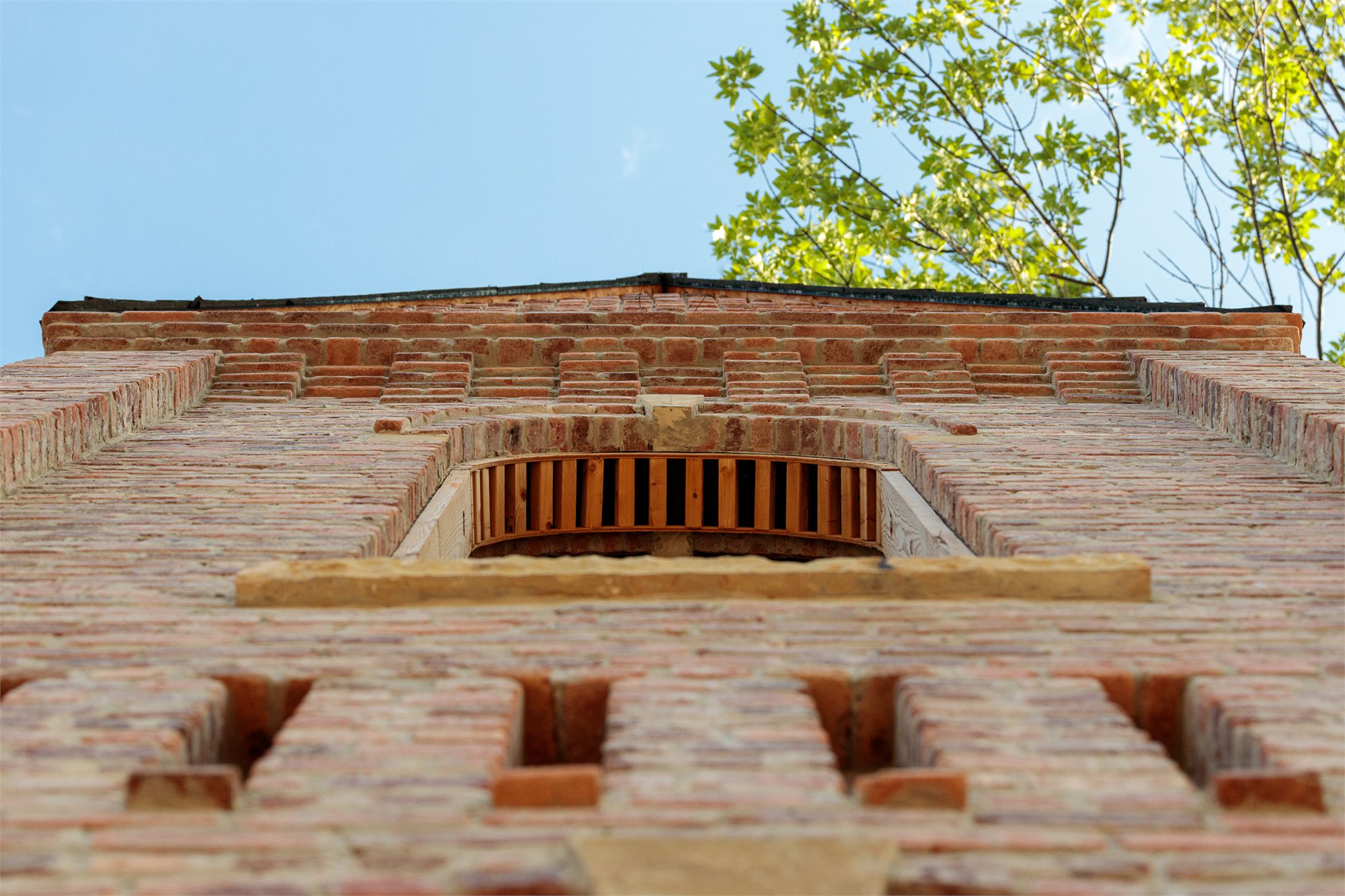 Looking up the corner of a Selah masonry tower — corbeled cornice and brick-lattice ventilation against open sky.