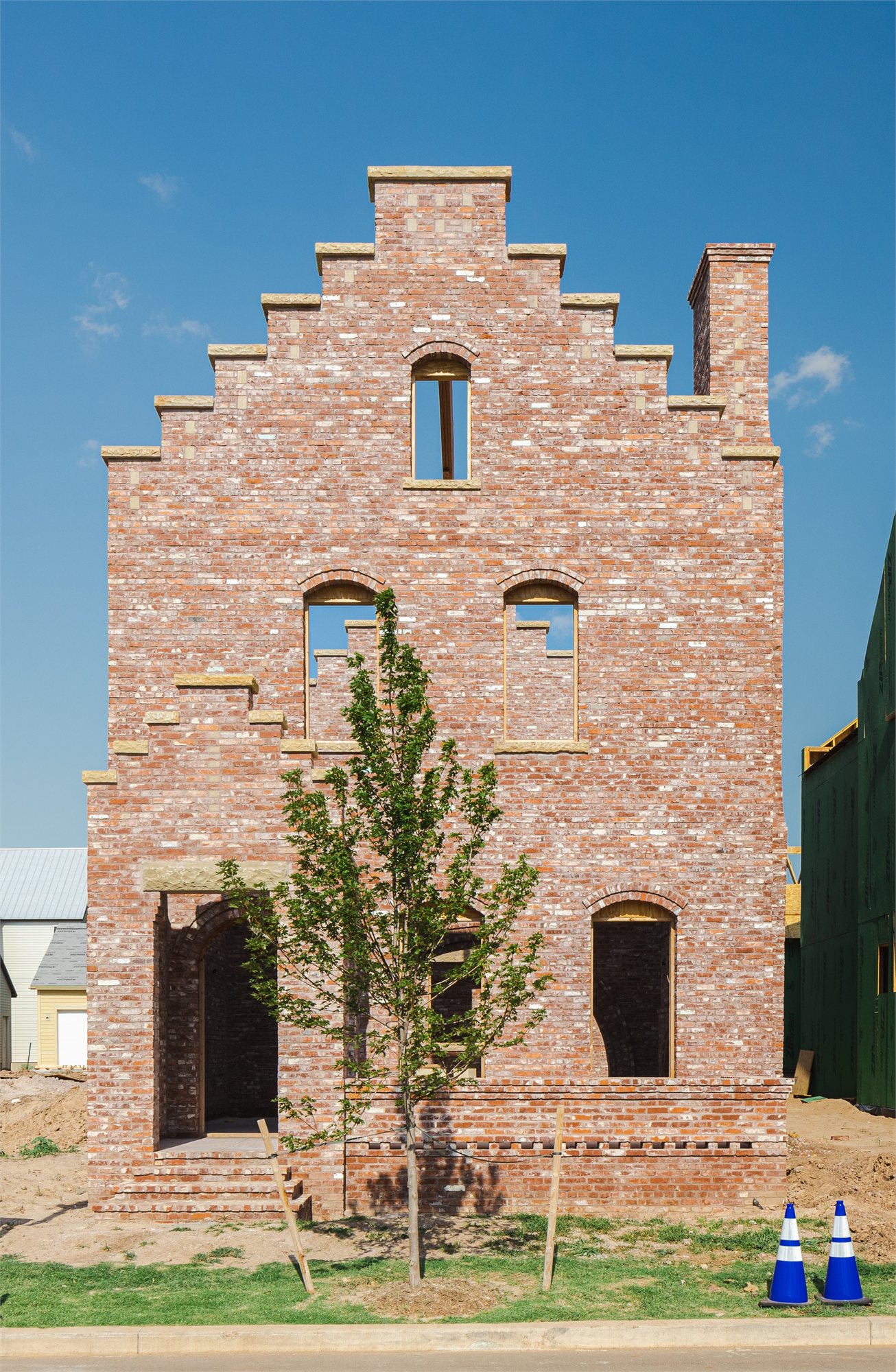 Stepped-gable brick facade with arched window openings and a young street tree at the front yard.