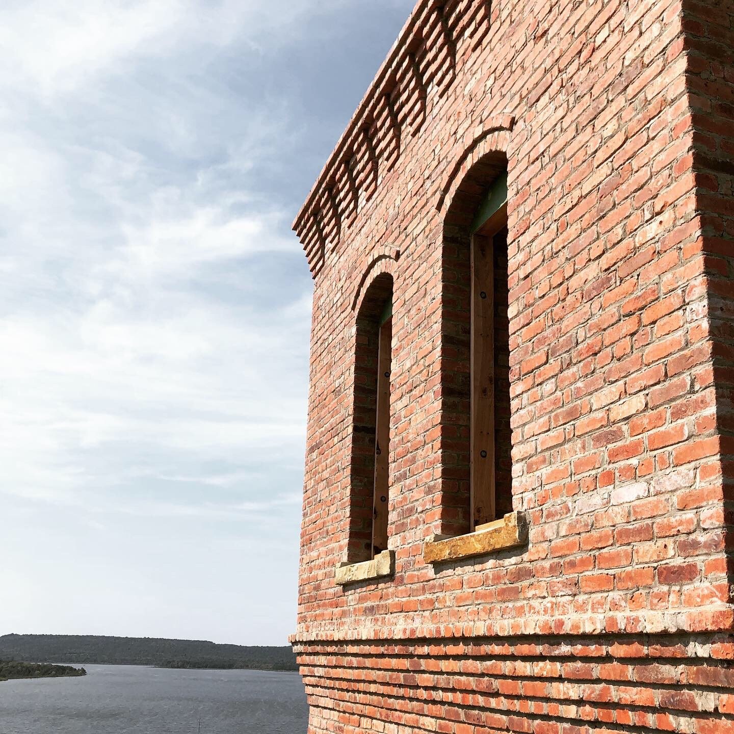 Masonry tower lookout corner — corbeled brick cornice and arched window slots, with water and shoreline beyond.