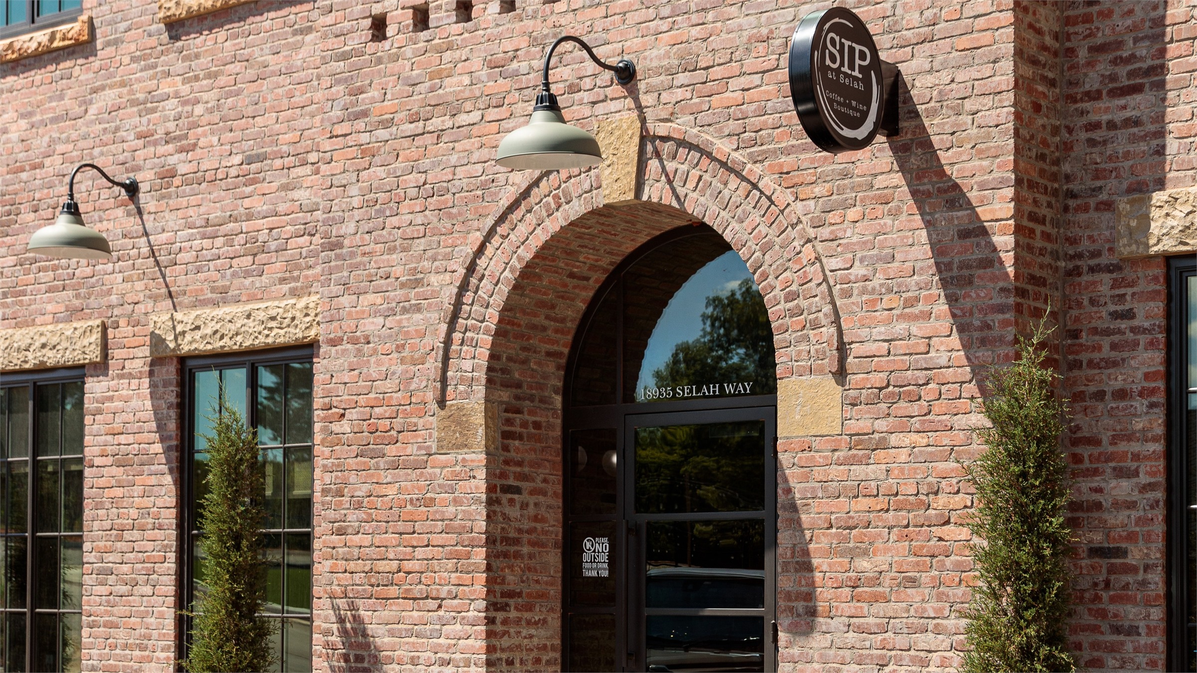 Arched brick threshold at SIP at Selah — gooseneck lamps and sandstone trim around a recessed entry door.