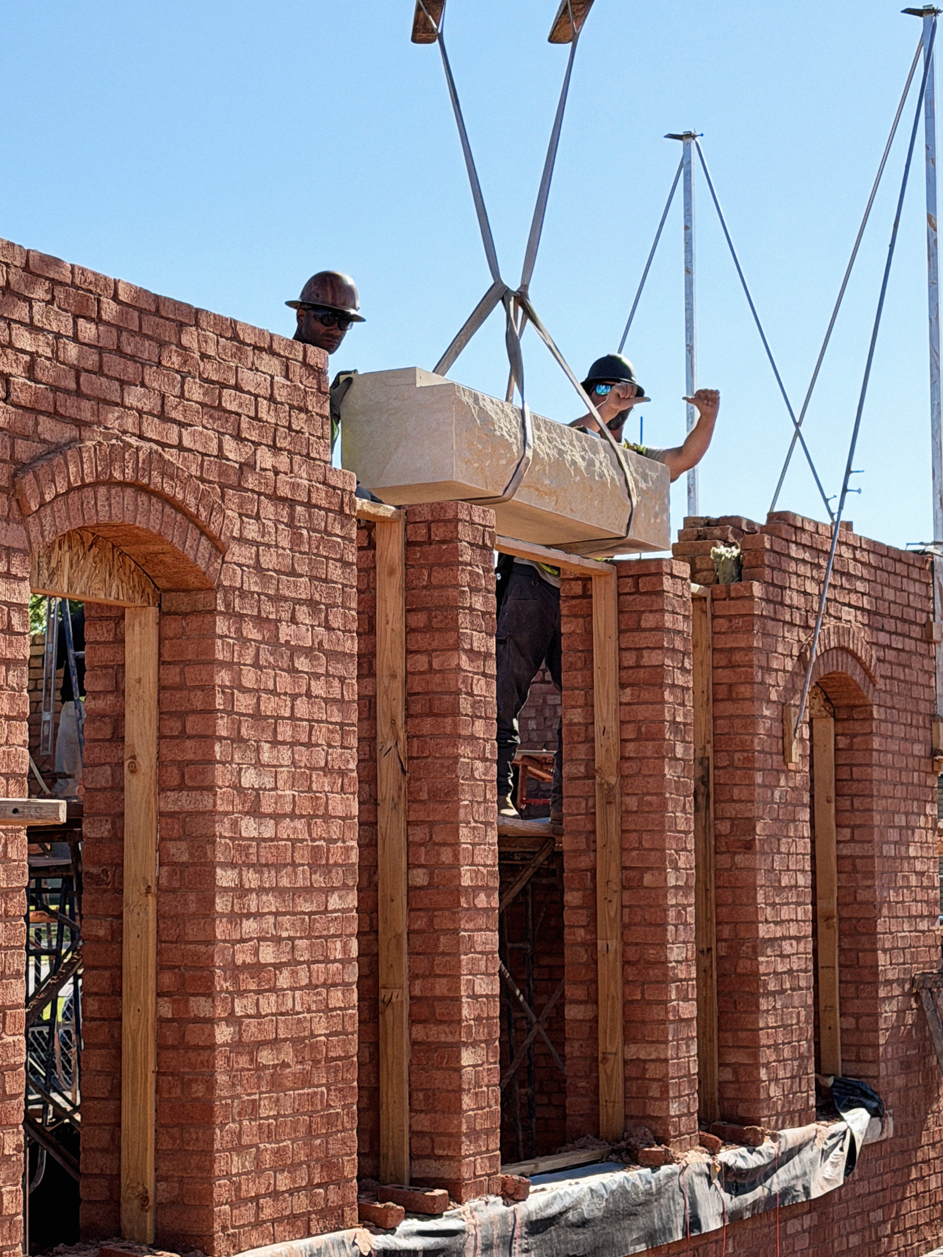 Building Culture masonry crew setting a stone lintel in a structural brick wall