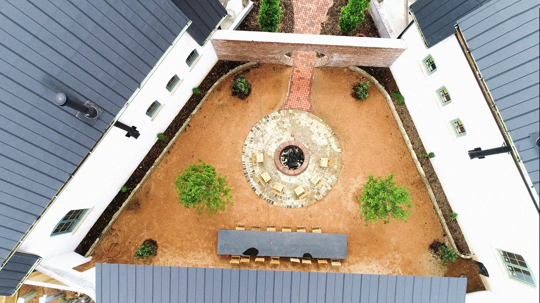 Aerial view of the Bend at Carlton Landing — two pitched-roof brick homes framing a shared garden courtyard with a central stone fire ring and a long communal table.